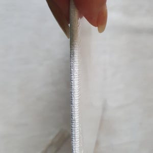 May include: Close-up of a white canvas print with a stitched edge. The canvas is held by a person, showing the side profile and texture of the material. The print appears to be stretched over a frame.