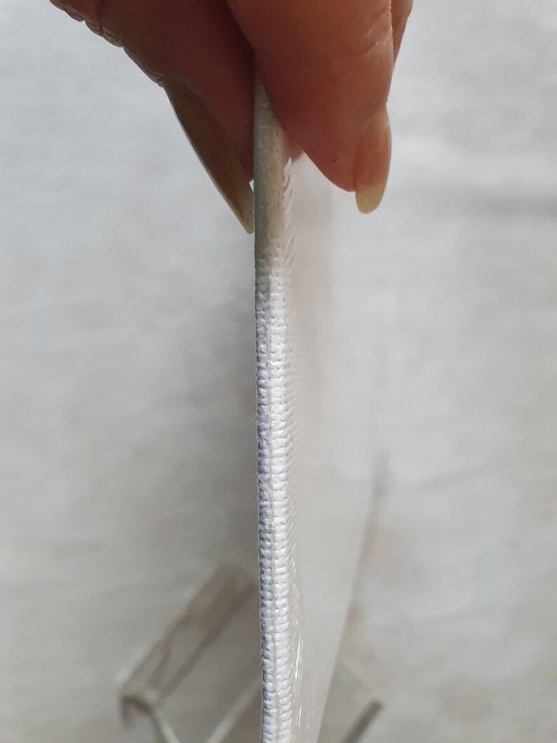 May include: Close-up of a white canvas print with a stitched edge. The canvas is held by a person, showing the side profile and texture of the material. The print appears to be stretched over a frame.