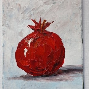 May include: Oil painting of a ripe pomegranate. The fruit is a vibrant red with textured brushstrokes, set against a white and light blue background. The painting captures the pomegranate's round shape and crown.