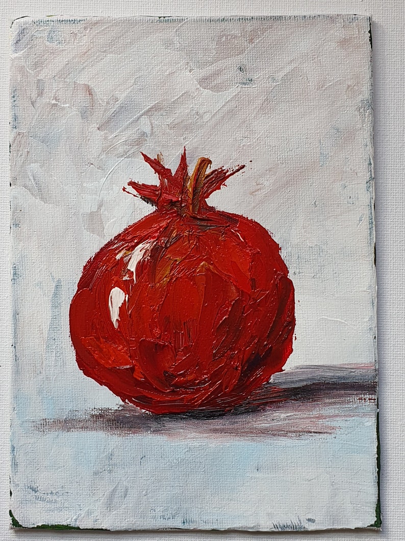 May include: Oil painting of a ripe pomegranate. The fruit is a vibrant red with textured brushstrokes, set against a white and light blue background. The painting captures the pomegranate's round shape and crown.