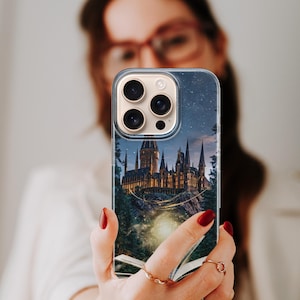 Phone case artwork showing a magical fantasy castle emerging from an open book placed on rocky ground. A soft golden light flows from the pages, illuminating the castle towers and surrounding mist. The scene is set at night with deep blue tones, glowing stars, and a dreamy atmosphere. The illustration combines elements of fantasy literature, imagination, and magic, creating a storybook-inspired design that feels warm, enchanting, and mystical.