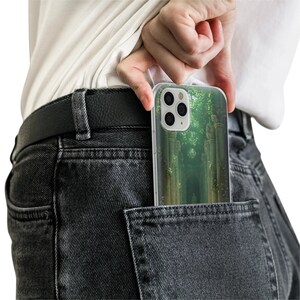 May include: A clear phone case with a green and white forest scene design. The case is in a back pocket of a pair of dark grey jeans.