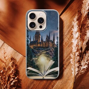 Phone case artwork showing a magical fantasy castle emerging from an open book placed on rocky ground. A soft golden light flows from the pages, illuminating the castle towers and surrounding mist. The scene is set at night with deep blue tones, glowing stars, and a dreamy atmosphere. The illustration combines elements of fantasy literature, imagination, and magic, creating a storybook-inspired design that feels warm, enchanting, and mystical.