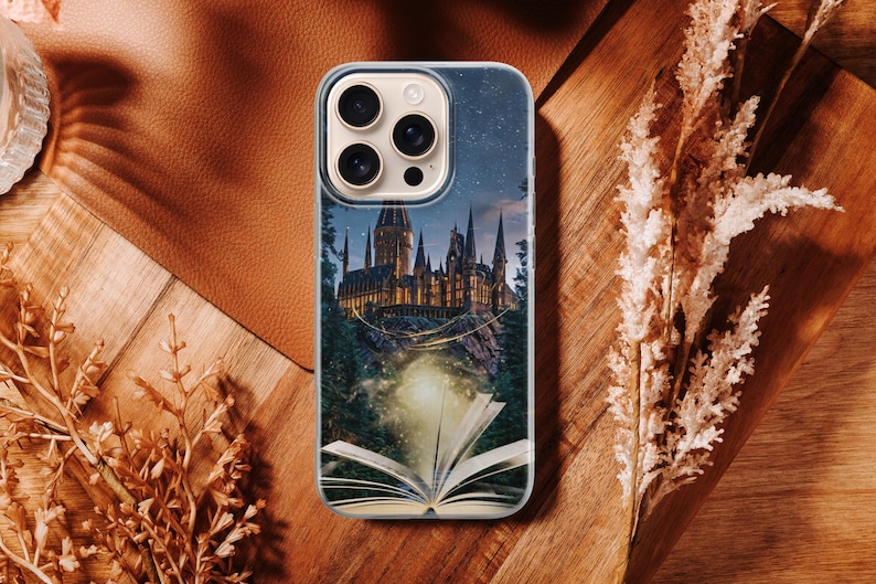 Phone case artwork showing a magical fantasy castle emerging from an open book placed on rocky ground. A soft golden light flows from the pages, illuminating the castle towers and surrounding mist. The scene is set at night with deep blue tones, glowing stars, and a dreamy atmosphere. The illustration combines elements of fantasy literature, imagination, and magic, creating a storybook-inspired design that feels warm, enchanting, and mystical.