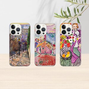 May include: Three phone cases with vibrant art prints. The first depicts a street scene with buildings and steps. The second shows a landscape with red roofs and blue sea. The third features a woman with flowers and fruit.