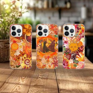 Op de afbeelding: Drie telefoonhoesjes met levendige bloemen- en hemelse ontwerpen. De hoesjes hebben een mix van oranje, gele en rode tinten, met afbeeldingen van vlinders, zonnen en bloemen. De hoesjes worden op een houten tafel getoond.