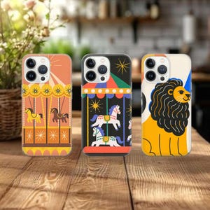 Op de afbeelding: Drie telefoonhoesjes met kleurrijke carrousel- en leeuwenontwerpen. De hoesjes hebben verschillende kleuren, waaronder oranje, zwart en geel. Elk hoesje heeft een ander ontwerp, met een carrousel, een leeuw en een carrousel.