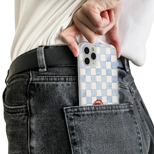 May include: A clear phone case with a blue and white checkered pattern is partially visible in a back pocket. The case has a watercolor design and a small illustration of a mouth. The phone case is being held by a person.