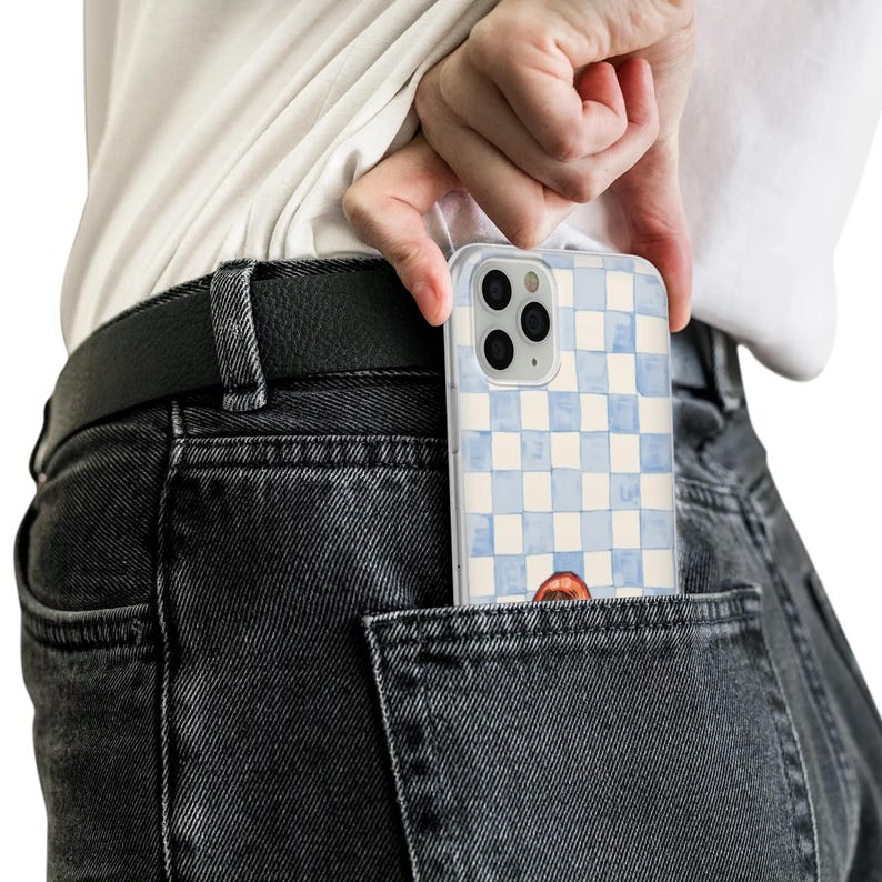 May include: A clear phone case with a blue and white checkered pattern is partially visible in a back pocket. The case has a watercolor design and a small illustration of a mouth. The phone case is being held by a person.