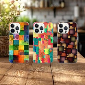 May include: Three colorful phone cases with geometric patterns. The cases are made of a clear material with a printed design. The designs feature squares and rectangles in various shades of red, orange, yellow, green, blue, and brown.