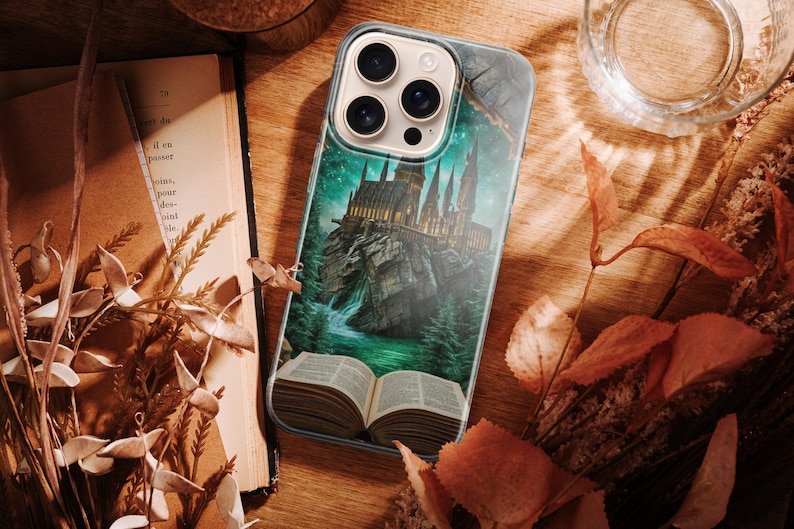 Fantasy-themed phone case featuring a majestic castle rising from an open book positioned on a rocky island. The scene is surrounded by glowing green and teal light, giving a magical and mysterious feeling. Tall castle towers reflect in the water below, while mist and light effects enhance the sense of fantasy and adventure. The illustration represents imagination, storytelling, and magical worlds coming to life from books.