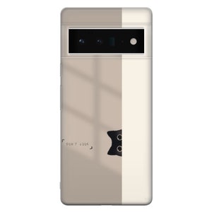 May include: A white and beige phone case with a black cat peeking out from behind a white stripe. The cat has two black eyes and a black nose. The text "DON'T LOOK" is printed on the case.