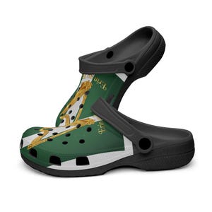 May include: Black and green clogs with a white stripe and a gold harp design. The clogs have a black strap and a green background with the word "Erin" in gold. The shoes are made of a rubber-like material.