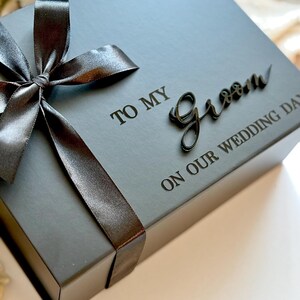 May include: A grey gift box tied with a dark grey satin ribbon and bow. The box is inscribed with the words "TO MY Groom ON OUR WEDDING DAY" in dark grey.
