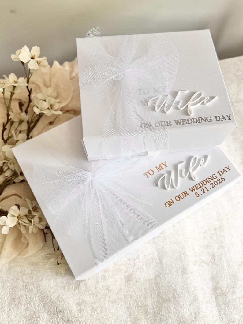 May include: Two white gift boxes with tulle bows. The top box reads "TO MY Wife ON OUR WEDDING DAY." The bottom box reads "TO MY Wife ON OUR WEDDING DAY 5.21.2026." The boxes are on a white surface.
