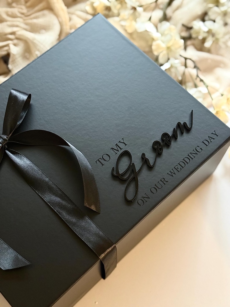 May include: A black gift box tied with a black satin ribbon. The box has the words "TO MY Groom ON OUR WEDDING DAY" in a script font.