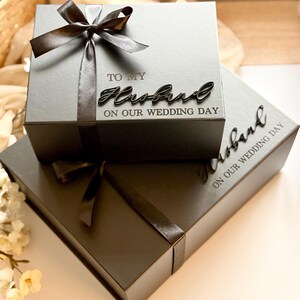 Puede incluir: Dos cajas de regalo grises, una encima de la otra, atadas con cintas de sat&eacute;n gris oscuro. La caja superior tiene las palabras "TO MY Husband ON OUR WEDDING DAY" en una fuente cursiva. La caja inferior tiene la palabra "Husband" y "ON OUR WEDDING DAY".