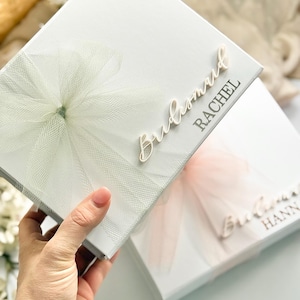 May include: White gift boxes with tulle accents. One box has "Bridesmaid Rachel" in script lettering. The other box has "Bridesmaid Hann" in script lettering. The boxes are decorated with tulle bows and are ideal for wedding gifts.