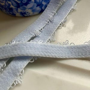 May include: Light blue elastic trim with a scalloped edge. The trim is soft and stretchy, and it would be perfect for adding a touch of elegance to any project.