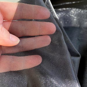 Könnte beinhalten: Nahaufnahme von schwarzem Mesh-Gewebe, das gegen das Licht gehalten wird und seine feine, gitterartige Struktur zeigt. Der Stoff ist leicht transparent und hat einen dezenten Glanz. Die Textur ist sichtbar, was auf ein leichtes Material hindeutet.