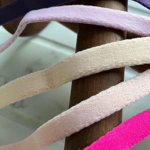 Può includere: Quattro nastri di colori diversi avvolti attorno a un  cilindro di legno. I colori dei nastri sono viola, rosa chiaro, beige e rosa acceso.