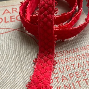 May include: Red elastic trim with a scalloped edge and a textured pattern. The trim is folded and coiled on a white surface.