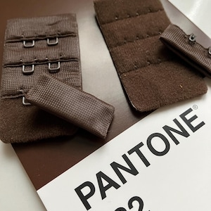 May include: Four brown bra strap extenders with hook and eye closures. The extenders are on a brown card with the text "PANTONE 732" printed in black.