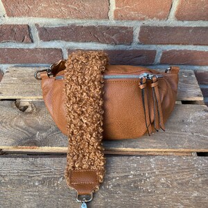 May include: A brown faux leather bum bag with a fluffy brown strap and a silver clasp. The bag has a zipper closure and a small tassel.