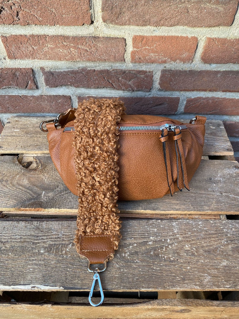 May include: A brown faux leather bum bag with a fluffy brown strap and a silver clasp. The bag has a zipper closure and a small tassel.