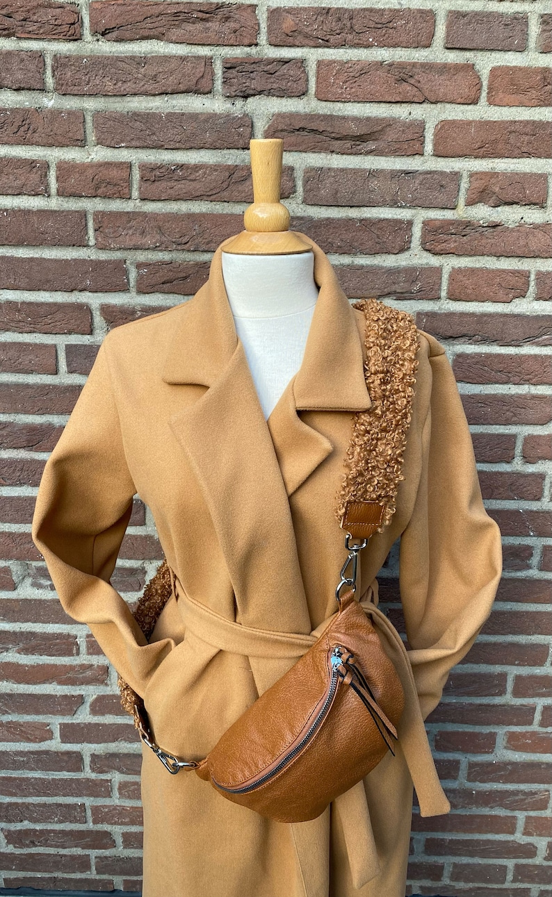 May include: A camel-coloured coat with a belt and a brown leather fanny pack with a fluffy strap.