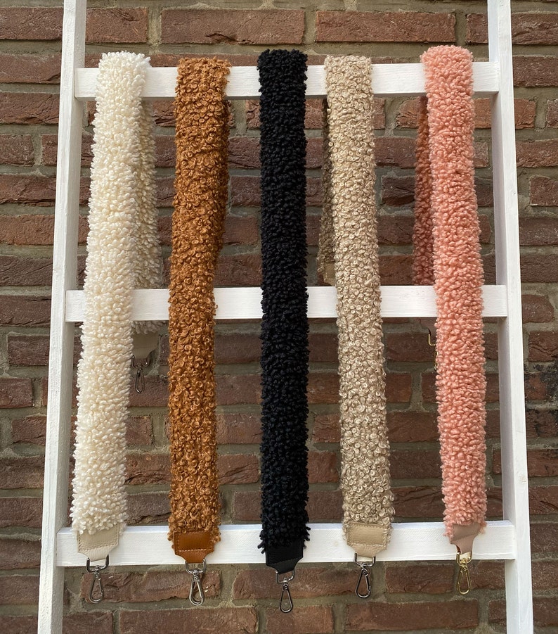 May include: Five different coloured fuzzy straps hanging on a white ladder. The straps are white, brown, black, beige, and pink.