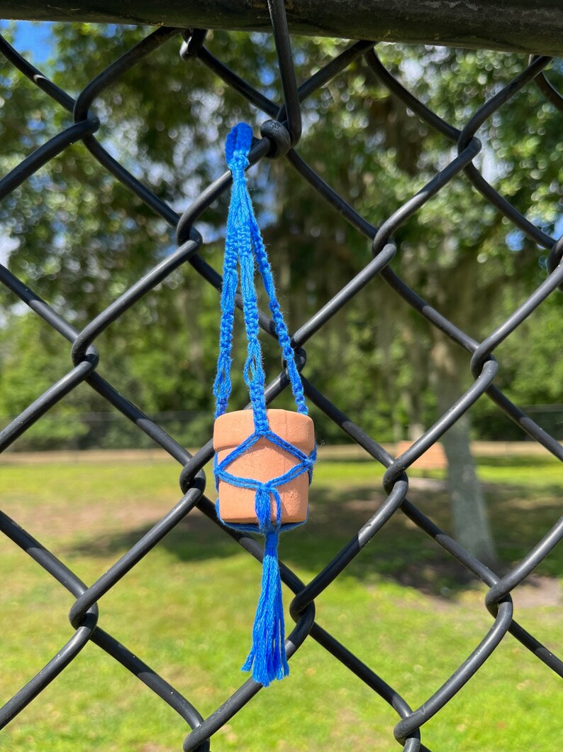 Puede incluir: Una peque&ntilde;a maceta de terracota con un macram&eacute; azul para colgar plantas, colgando de una valla de cadena de eslabones negra.