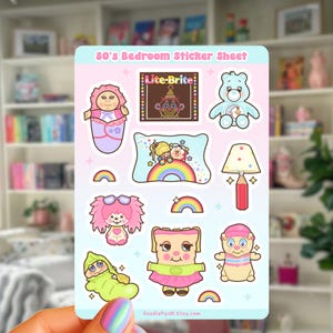 May include: A sticker sheet titled 80's Bedroom Sticker Sheet featuring illustrations of a swaddled doll, a Lite-Brite toy, a blue bear, a rainbow pillow, a pencil-shaped lamp, a pink-haired creature, a pea pod doll, and a small character.
