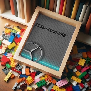 Peut inclure: Un cadre en bois avec un fond gris et un logo bleu et blanc. Le logo est un logo stylisé Mercedes-Benz avec le texte "AMG" au-dessus. Le cadre est entouré de blocs de construction en plastique colorés.