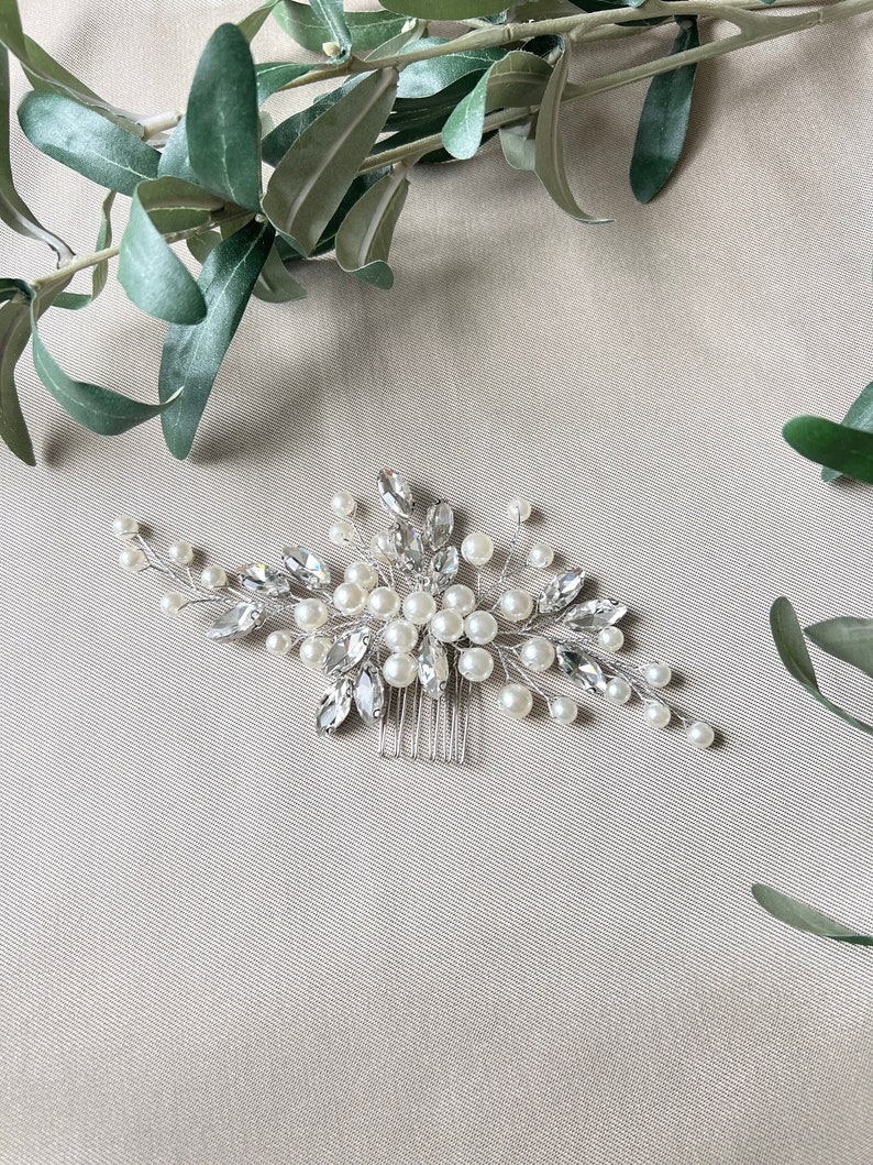 Wunderschöner Brauthaarkamm in Silber, verziert mit weißen Perlen und Strasssteinen für eine elegante Note. Ca. 15 cm lang und 7 cm breit. Die funkelnden Strasssteine werten jede Frisur auf. Perfekt für Braut, Trauzeuginnen und Brautjungfern