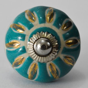 Peut inclure: Bouton de porte en céramique bleu sarcelle avec un centre blanc et des accents dorés. Le bouton a un centre en métal argenté.