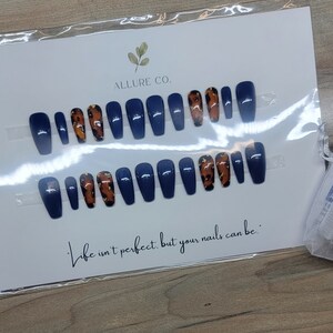 May include: A set of 10 blue and brown press-on nails with a leopard print design. The nails are displayed on a white card with the text "ALLURE CO." and "Life isn't perfect, but your nails can be."