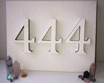 May include: White canvas with the number 444 painted in white on it. The canvas is textured and has a rough surface. There are small crystals scattered around the canvas.