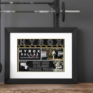 May include: A framed print with the word "HYROX" at the top. The print features the text "HYROX DALLAS" and "RODY GRIM 11.22.2025 DALLAS, TEXAS". The print is in a black frame and is displayed on a wooden surface with gym equipment in the background.