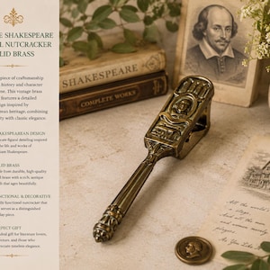 May include: A solid brass nutcracker featuring an intricate figural design inspired by William Shakespeare. The tool has a long, detailed handle and a rectangular head with embossed imagery. A small matching brass coin sits nearby on the surface.