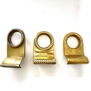 May include: Three antique brass drawer pulls. Each pull features a rectangular base with a decorative edge and a circular handle. The handles have a rope-like texture. The brass has a warm, aged patina.