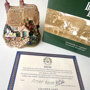 Puede incluir: Figura en miniatura de una casa de campo con tejado de paja, detalles de mampostería y acentos florales coloridos. La figura va acompañada de una caja verde y una escritura de propiedad de Lilliput Lane, hecha a mano en Inglaterra.