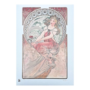 May include: A vintage art nouveau print featuring a woman in a pink dress with a floral design. The woman is surrounded by a decorative frame with a circular pattern.