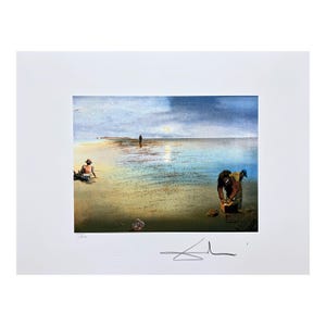 Puede incluir: Una lámina de arte montada en paspartú que muestra un paisaje costero con playa de arena, mar en calma y cielo nublado. Tres figuras son visibles en la orilla, una de ellas arrodillada junto a una caja. Una firma aparece en el margen inferior.