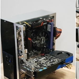 Könnte beinhalten: Ein silbernes Computergehäuse mit einem schwarzen Motherboard, einer Grafikkarte und einem Lüfter. Das Gehäuse ist geöffnet und die Komponenten sind sichtbar. Das Gehäuse steht auf einem Holztisch.