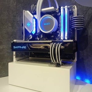 Könnte beinhalten: Ein weißes Computergehäuse mit einer transparenten Acrylseitenteil, das einen selbstgebauten PC mit einem weißen Motherboard, einem weißen NZXT-Wasserkühler und einer schwarzen und blauen Sapphire-Grafikkarte zeigt. Das Gehäuse ist mit blauen LED-Lichtern beleuchtet.