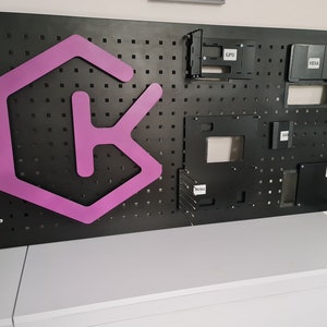 Op de afbeelding: Een zwart prikbord met een roze "K"-logo en verschillende zwarte metalen opbergvakken met de labels "CPU", "VGA", "HDD" en "PSU".
