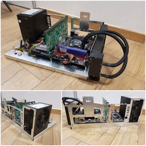 Könnte beinhalten: Ein kundenspezifisches Computergehäuse mit verschiedenen sichtbaren Komponenten. Das Gehäuse aus silberfarbenem Metall beherbergt ein Motherboard, eine Grafikkarte, ein Netzteil und ein Kühlsystem. Der Text "F-CASE" ist auf der Seite sichtbar. Die Komponenten sind auf einer silberfarbenen Metallbasis angeordnet.