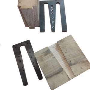 May include: Two sets of light-coloured wooden blocks paired with dark grey metal U-shaped brackets. Each metal bracket features a series of circular holes along the centre spine. The wood pieces have a rectangular shape with visible grain patterns.