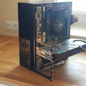Può includere: Un case per computer nero con un pannello laterale trasparente, che rivela la scheda madre, la scheda grafica e altri componenti. Il case è posizionato su una superficie di legno.